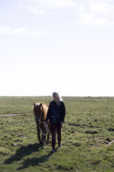 Frau mit Pferd in voller Länge auf einem grasbewachsenen Feld gegen den Himmel an einem sonnigen Tag - CAVF61593