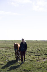 Full length of woman with horse walking on grassy field against sky during sunny day - CAVF61593