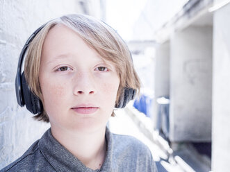 Porträt eines Jungen in Nahaufnahme, der an einer Wand stehend Musik hört - CAVF61598
