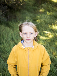 Hochwinkliges Porträt eines ernsthaften Jungen in warmer Kleidung, der auf einer Wiese im Park steht - CAVF61600
