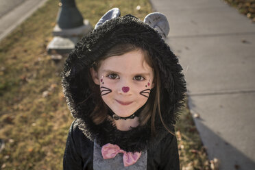 Porträt eines niedlichen Mädchens im Katzenkostüm auf dem Rasen während Halloween - CAVF61638