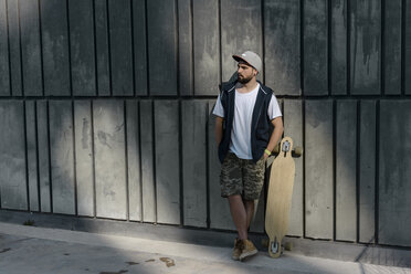 Nachdenklicher Mann mit Skateboard an einer Betonwand stehend - CAVF61649