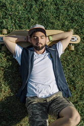 Hoher Winkel Blick auf gut aussehende Mann mit Skateboard auf grasbewachsenen Feld im Park liegen - CAVF61654