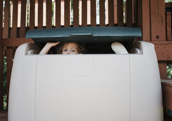 Porträt eines niedlichen Mädchens, das sich auf dem Spielplatz in einer Schachtel versteckt - CAVF61717