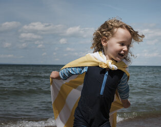 Glückliches Mädchen mit Umhang beim Laufen am Meer gegen den Himmel an einem sonnigen Tag - CAVF61725