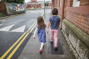 Rear view of siblings holding hands while walking at sidewalk in city - CAVF61731