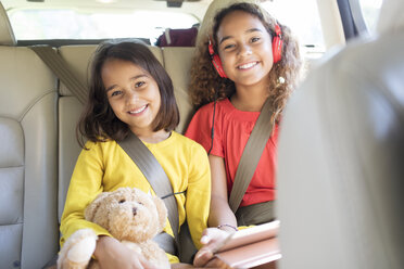 Portrait happy sisters with teddy bear riding in back seat of car - CAIF22809