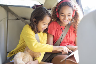 Schwestern benutzen digitales Tablet auf dem Rücksitz eines Autos - CAIF22812