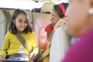 Glückliche Schwestern auf dem Rücksitz eines Autos mit digitalem Tablet - CAIF22816