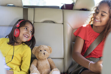 Glückliche Schwestern und Teddybär auf dem Rücksitz eines Autos - CAIF22820
