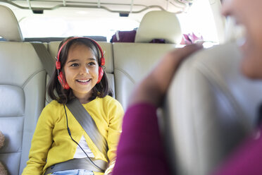 Lächelndes Mädchen mit Kopfhörern auf dem Rücksitz eines Autos - CAIF22821