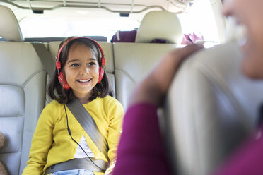 Smiling girl with headphones riding in back seat of car - CAIF22821