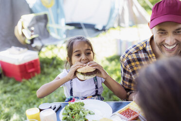 Father and daughter eating barbecue hamburgers at campsite - CAIF22831