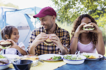 Glücklicher Vater und Töchter essen Hamburger vom Grill auf dem Campingplatz - CAIF22844