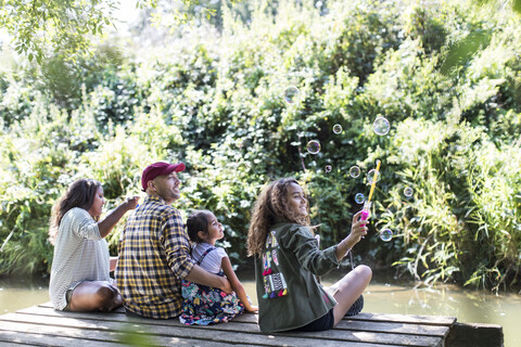 Familie bläst Seifenblasen am Steg im Wald, lizenzfreies Stockfoto