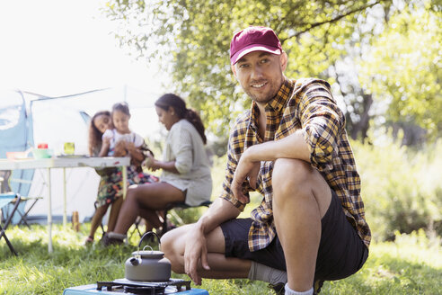 Porträt eines selbstbewussten Mannes, der eine Teekanne auf einem Campingkocher auf einem sonnigen Campingplatz erhitzt - CAIF22848