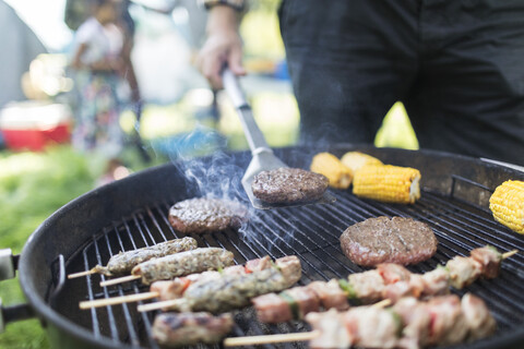 Mann beim Grillen von Hamburgern, Spießen und Maiskolben, lizenzfreies Stockfoto