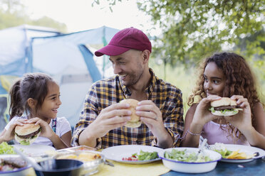 Vater und Töchter genießen einen Hamburger vom Grill auf dem Campingplatz - CAIF22857