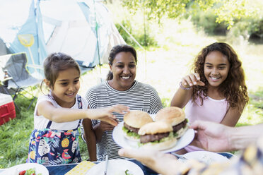 Glückliche Mutter und Töchter greifen auf dem Campingplatz nach gegrillten Hamburgern - CAIF22858