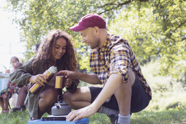 Tochter schenkt ihrem Vater am Campingkocher Kaffee aus einem isolierten Getränkebehälter ein - CAIF22864