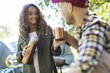 Tochter schenkt ihrem Vater auf dem Campingplatz Kaffee aus einem isolierten Getränkebehälter ein - CAIF22865