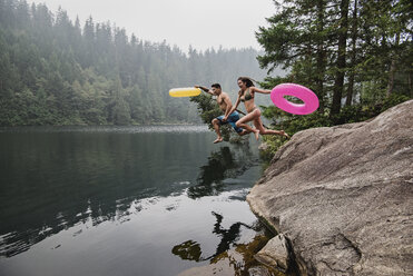 Verspieltes junges Paar mit aufblasbaren Ringen, das in einen abgelegenen See springt, Squamish, British Columbia, Kanada - CAIF22885