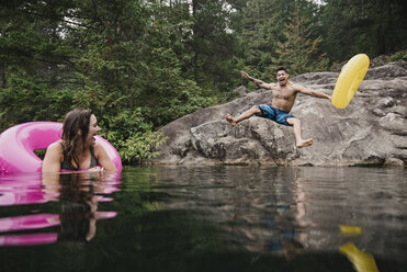 Verspielter junger Mann mit aufblasbarem Ring, der in einen abgelegenen See springt, Squamish, British Columbia, Kanada - CAIF22887