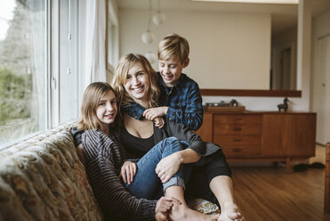 Portrait happy mother and children cuddling on living room sofa - CAIF22893