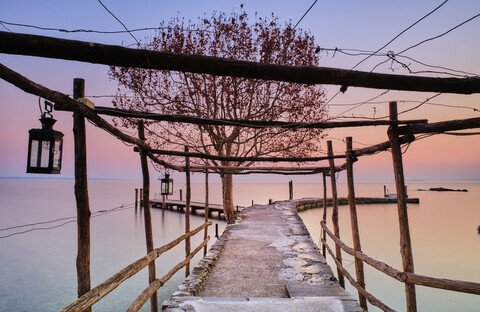 Italien, Punta san Vigilio, Gardasee, Steg und Baum im Winter bei Sonnenuntergang, lizenzfreies Stockfoto