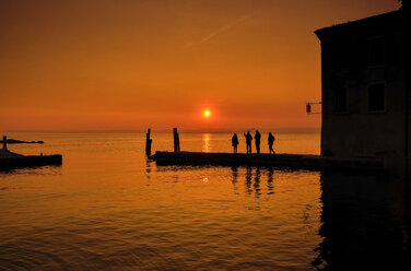 Italien, Punta san Vigilio, Silhouetten von vier Personen auf dem Bootssteg bei Sonnenuntergang über dem Gardasee im Winter - MRF01932