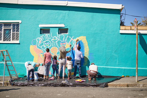 Freiwillige aus der Gemeinde malen ein lebendiges Wandgemälde auf eine sonnige Stadtmauer - CAIF22898