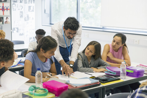 Ein männlicher Lehrer hilft einer Schülerin am Schreibtisch im Klassenzimmer, lizenzfreies Stockfoto