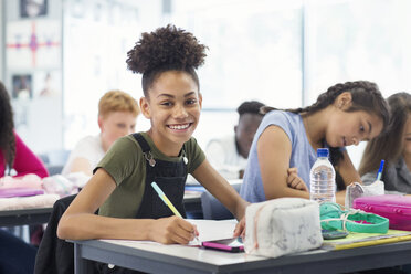 Portrait confident junior high school girl student doing homework in classroom - CAIF22922