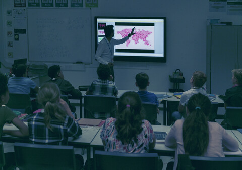 Schüler beobachten den Geografielehrer auf der Projektionsfläche im dunklen Klassenzimmer, lizenzfreies Stockfoto