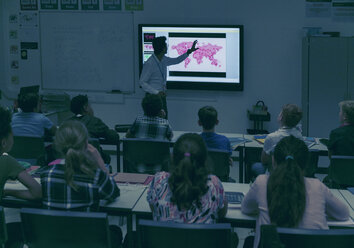 Schüler beobachten den Geografielehrer auf der Projektionsfläche im dunklen Klassenzimmer - CAIF22928