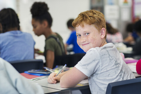 Porträt lächelnd, zuversichtlich Junior High School Junge Student studiert am Schreibtisch im Klassenzimmer, lizenzfreies Stockfoto