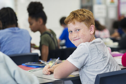 Porträt lächelnd, zuversichtlich Junior High School Junge Student studiert am Schreibtisch im Klassenzimmer - CAIF22936