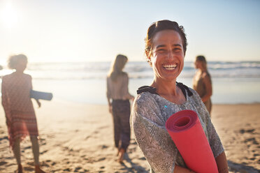 Portrait glückliche Frau mit Yogamatte am sonnigen Strand während eines Yoga-Retreats - CAIF22946