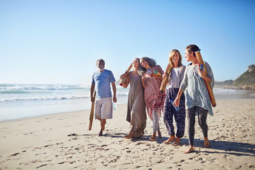 Friends walking with yoga mats on sunny beach during yoga retreat - CAIF22953