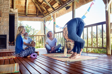 Yogalehrerin demonstriert die Vorwärtsfalte in einer Hütte während eines Yoga-Retreats - CAIF22954