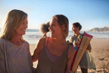 Glückliche Mutter und Tochter mit Yogamatte am sonnigen Strand während eines Yoga-Retreats - CAIF22961