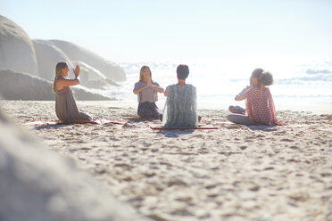 Group meditating in circle on sunny beach during yoga retreat - CAIF22963