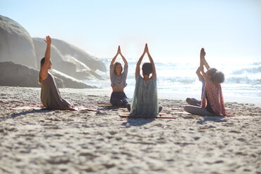 Serene people in circle meditating on sunny beach during yoga retreat - CAIF22964
