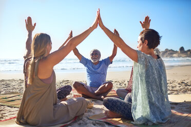 Group joining hands in circle on sunny beach during yoga retreat - CAIF22968