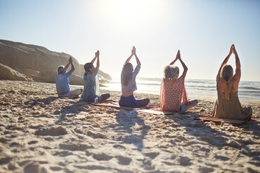 Group practicing yoga on sunny beach during yoga retreat - CAIF22976