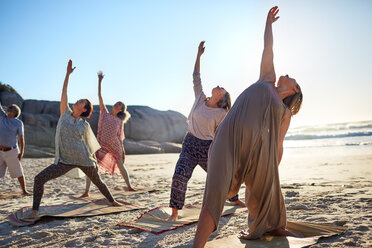 Gruppe beim Üben der umgekehrten Kriegerpose am sonnigen Strand während eines Yoga-Retreats - CAIF22979