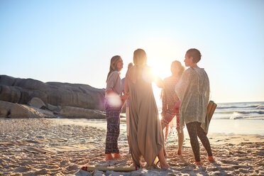 Women standing in circle on sunny beach during yoga retreat - CAIF22981