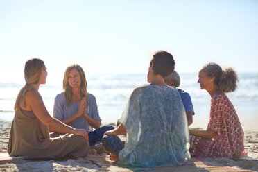 Happy friends talking in circle on sunny beach during yoga retreat - CAIF22985