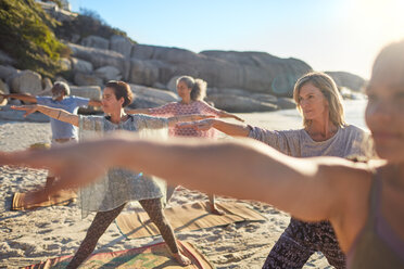 Group practicing yoga on sunny beach during yoga retreat - CAIF22986