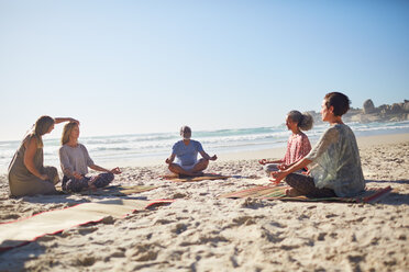 Group meditating on sunny beach during yoga retreat - CAIF22988